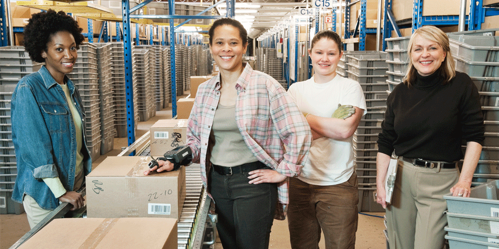 Four women in a factory setting smiling.